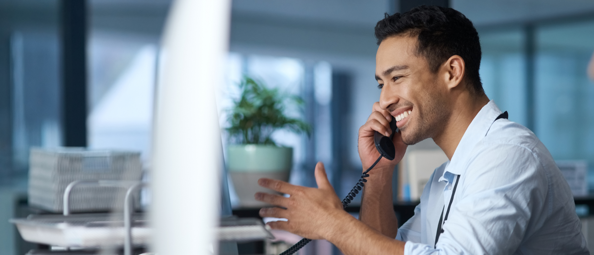 Smiling man speaking on a landline phone in a modern office, providing customer support.